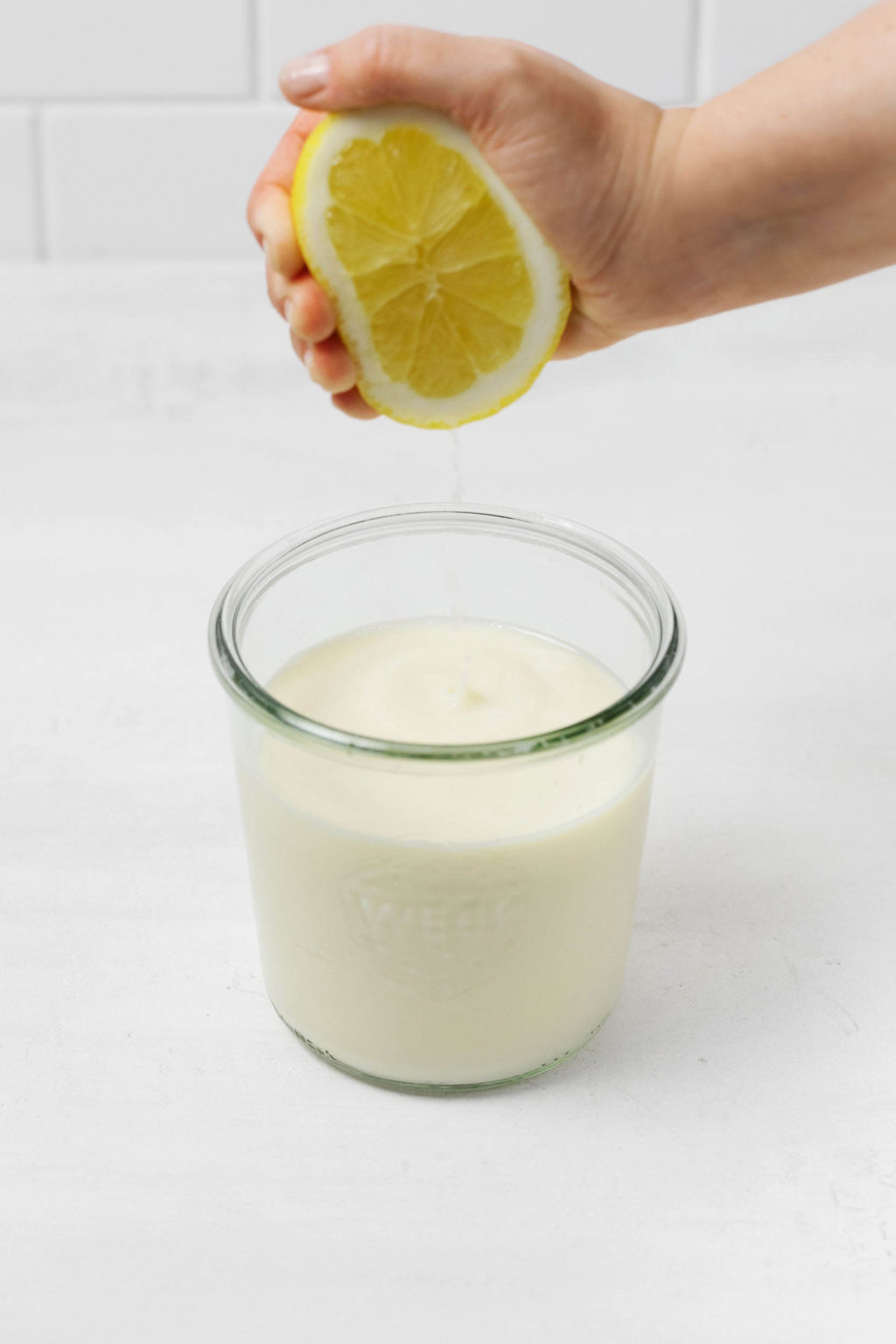 A lemon is being squeezed into a mason jar full of milk. It rests on a white surface.
