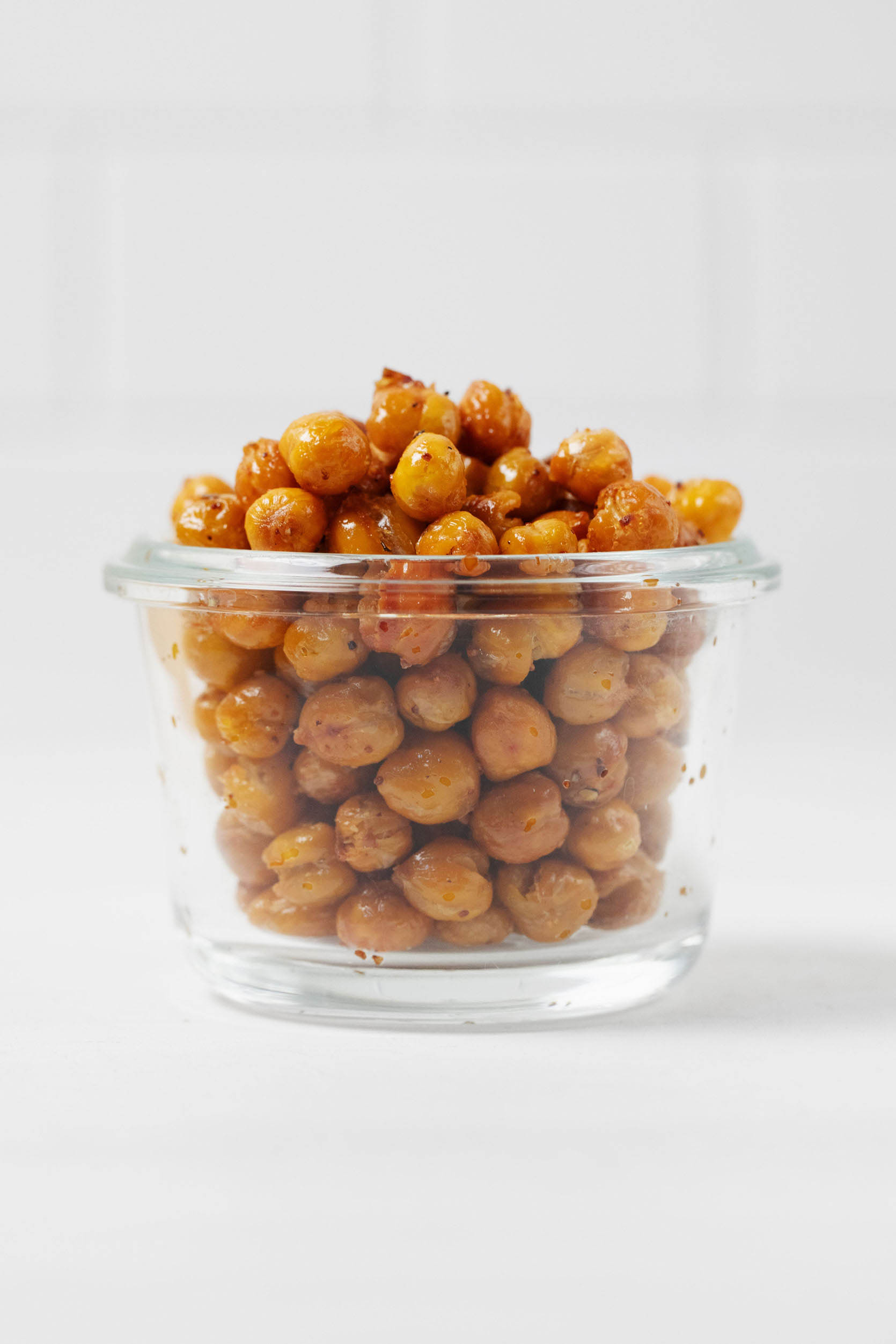 A glass, Weck mason jar is filled with golden, crispy roasted chickpeas. A white tiled surface is visible behind the jar.
