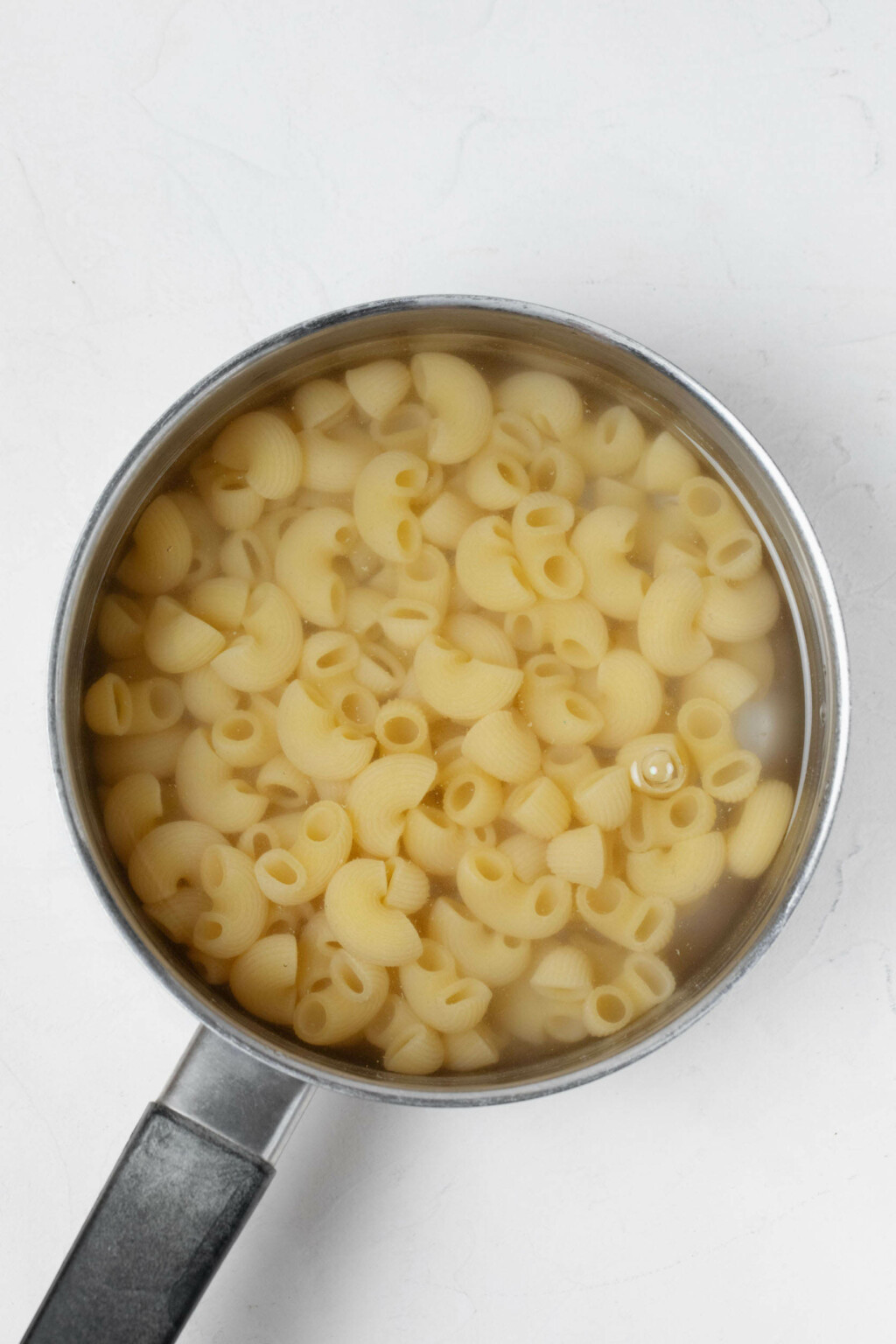 A silver pot of water is being used to boil small pasta shells.