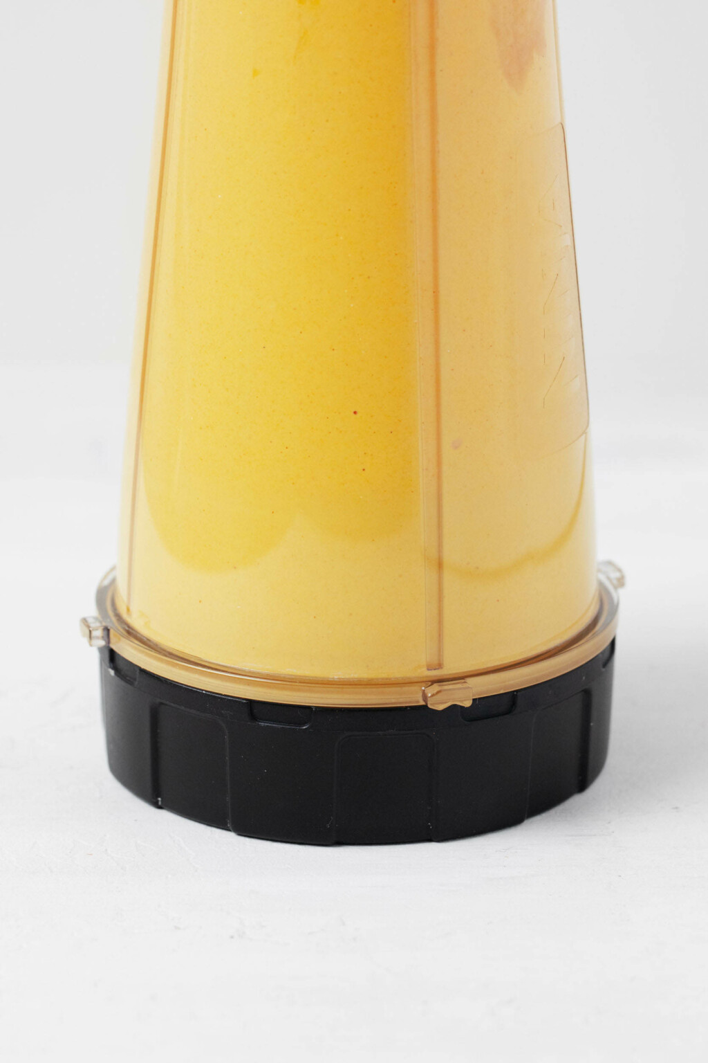 A personal blender is being used to blend a bright yellow colored sauce.